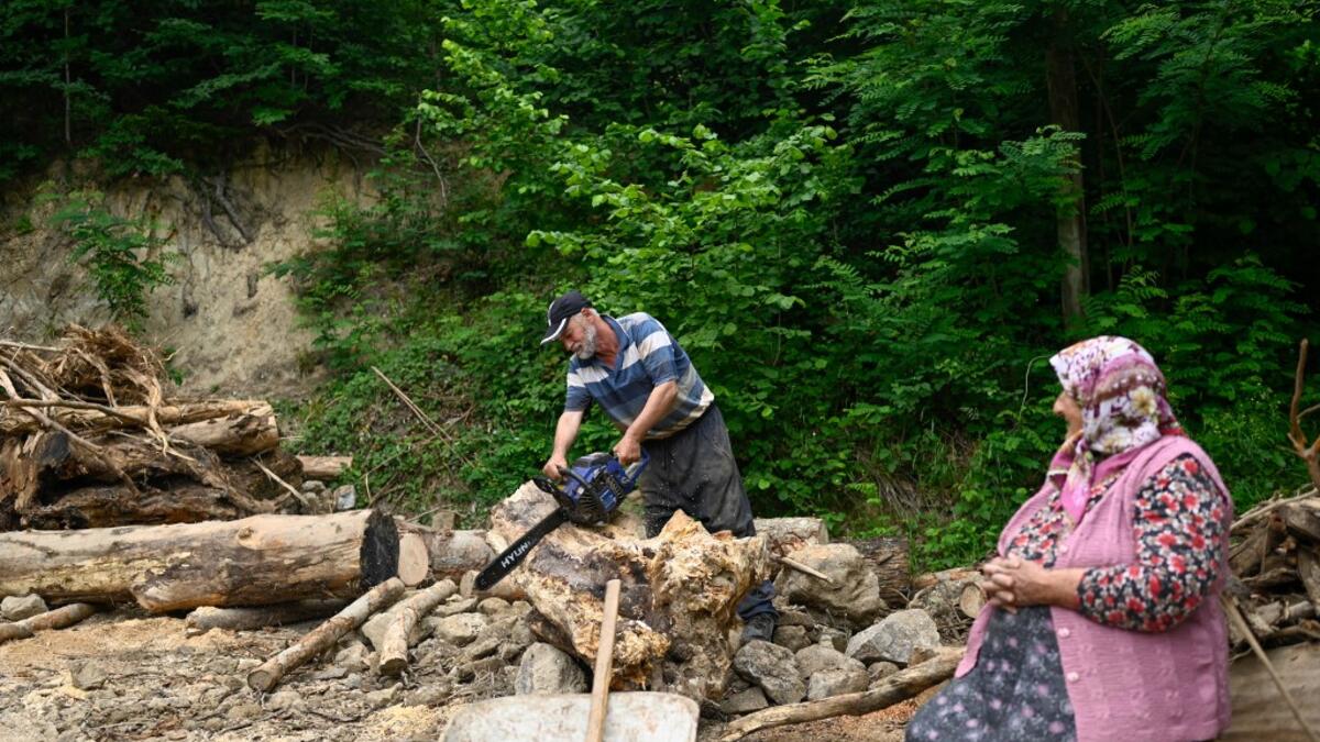 A villager saws wood as a woman looks on in Ikizdere in Rize Province in the Black Sea region of Turkey on June 7, 2021. A government-friendly company plans to extract 20 million tons of stone from a quarry in the northeastern town of Ikizdere for one of President Recep Tayyip Erdogan's latest development projects. The locals are rising up in protest, challenging the government and its priorities in a region dear to the domineering Turkish leader's heart.