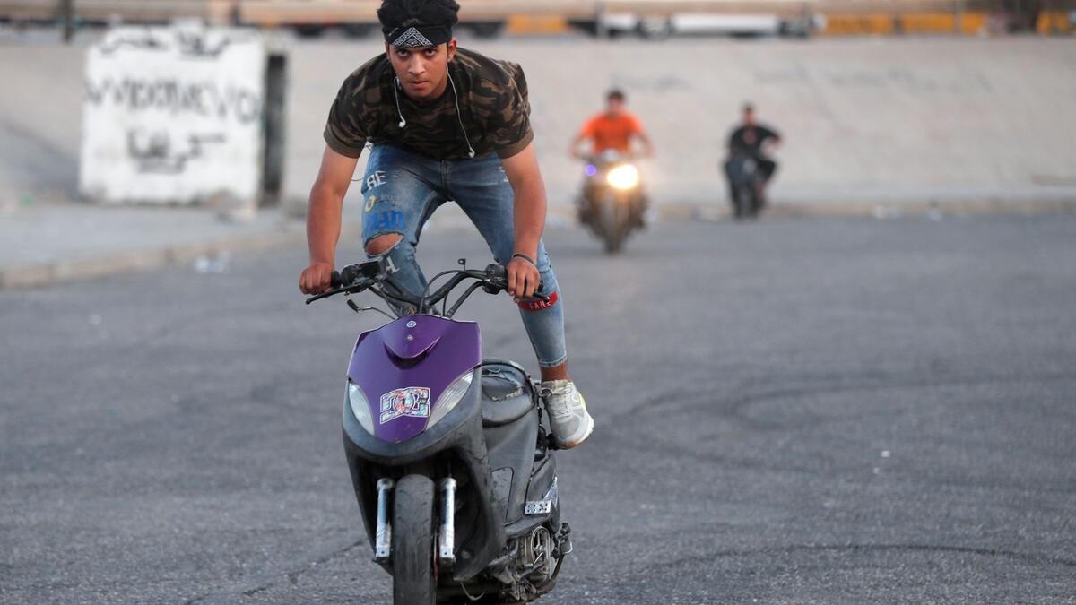 Iraqi youths perform stunts on their scooters in the Jadriya district of Baghdad on August 6, 2021. All dressed up and nowhere to go: many young Iraqis in Baghdad make an effort to be hip, even as they admit their country may have no future.