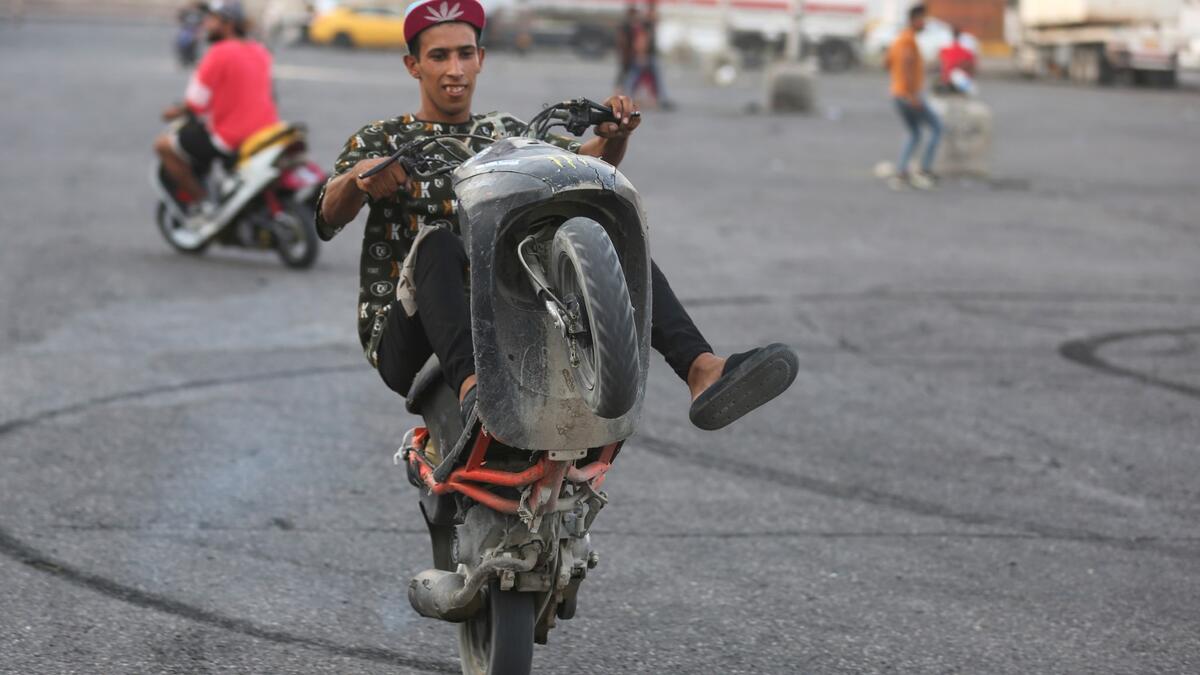 Iraqi youths perform stunts on their scooters in the Jadriya district of Baghdad on August 6, 2021. All dressed up and nowhere to go: many young Iraqis in Baghdad make an effort to be hip, even as they admit their country may have no future.