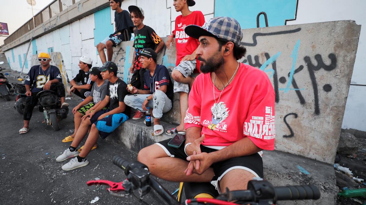 Iraqi youths watch others perform stunts on motorbikes and scooters in the Jadriya district of Baghdad on August 6, 2021. All dressed up and nowhere to go: many young Iraqis in Baghdad make an effort to be hip, even as they admit their country may have no future.