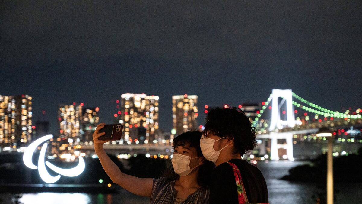 This picture taken on August 21, 2021 shows people taking pictures before the Paralympic Games symbol lit up at night on the Odaiba waterfront in Tokyo.