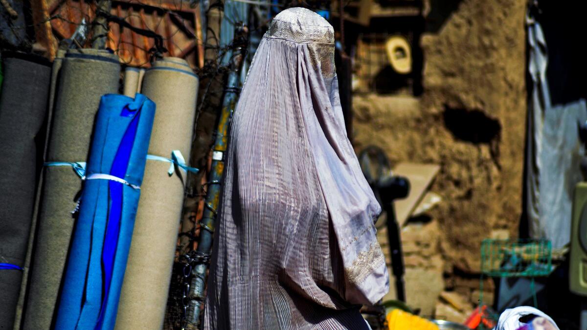 CORRECTION / A burqa-clad woman walks past a stall selling secondhand items at a market in Kandahar on September 22, 2021.