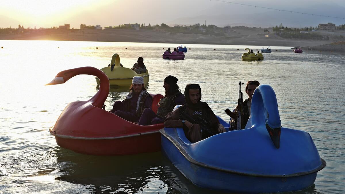 In this photograph taken on September 28, 2021 Taliban fighters ride on paddle boats at Qargha Lake on the outskirts of Kabul. "This is Afghanistan!" a Taliban fighter shouts on the pirate ship ride at a fairground in western Kabul, as his armed comrades cackle and whoop on board the rickety attraction. (Photo by WAKIL KOHSAR / AFP) / TO GO WITH: AFGHANISTAN-CONFLICT-FAIRGROUND, SCENE BY JAMES EDGAR - TO GO WITH: Afghanistan-conflict-fairground, SCENE by James EDGAR