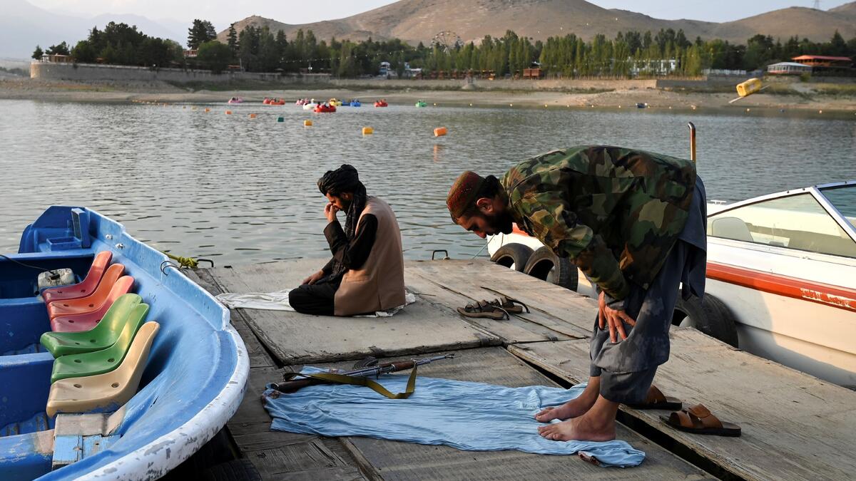Taliban fighters offer prayers on a dock for boats at Qargha Lake on the outskirts of Kabul. "This is Afghanistan!" a Taliban fighter shouts on the pirate ship ride at a fairground in western Kabul, as his armed comrades cackle and whoop on board the rickety attraction. (Photo by WAKIL KOHSAR / AFP) / TO GO WITH: AFGHANISTAN-CONFLICT-FAIRGROUND, SCENE BY JAMES EDGAR - TO GO WITH: Afghanistan-conflict-fairground, SCENE by James EDGAR