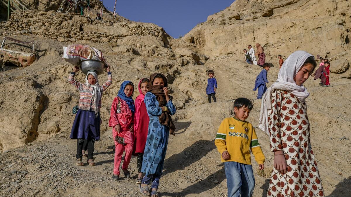 In this picture taken on October 3, 2021, children walk to a river from their village near the cliffs pockmarked by caves where people still live as they did centuries ago in Bamiyan.
