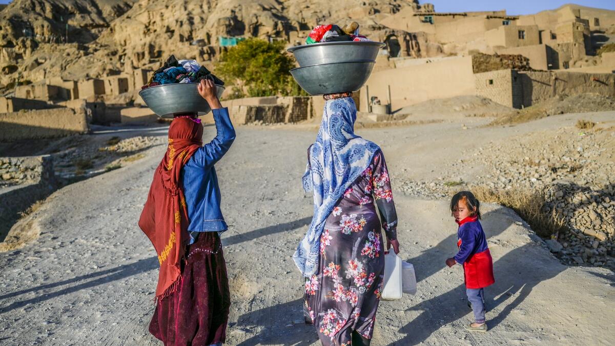 In this picture taken on October 3, 2021, Hazara ethnic women walk with their laundry to their village near the cliffs pockmarked by caves where people still live as they did centuries ago in Bamiyan.