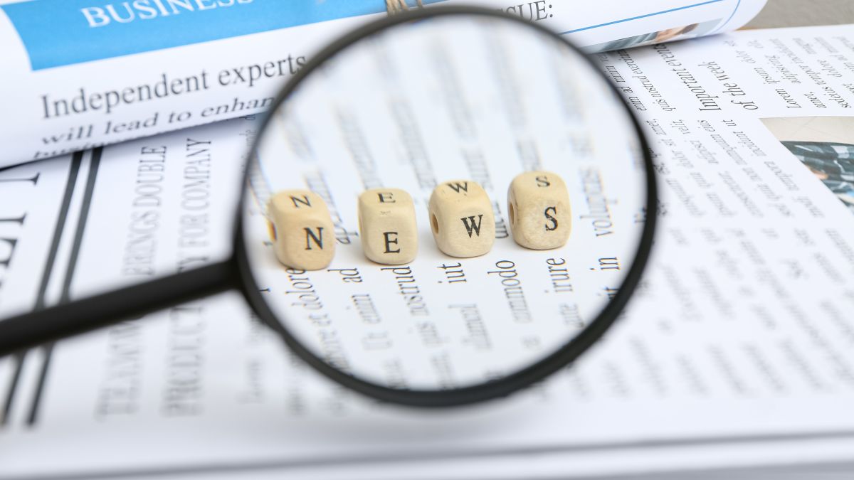 عدسة مكبرة فوق صحيفة تحمل كلمة "News"، في صورة تعبيرية عن متابعة الأخبار ووسائل الإعلام