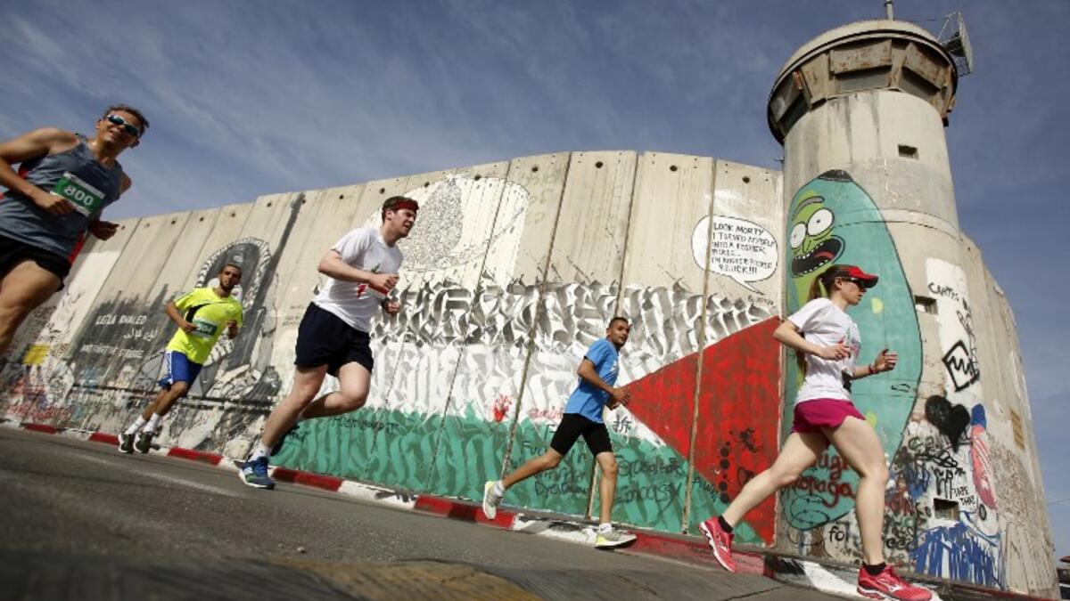 Participants run along Israel's controversial separation barrier, which divides the West Bank from Jerusalem, in the biblical town of Bethlehem during the 6th International Palestine Marathon on Mar. 23, 2018. 
(Musa AL SHAER / AFP)
