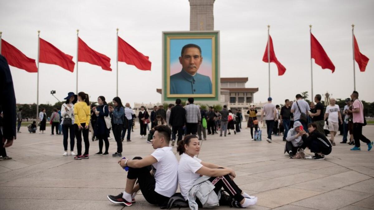 A couple sit back-to-back past a portrait of nationalist leader Sun Yat-sen in Tiananmen Square on the May Day holiday in Beijing on May 1, 2018 / AFP