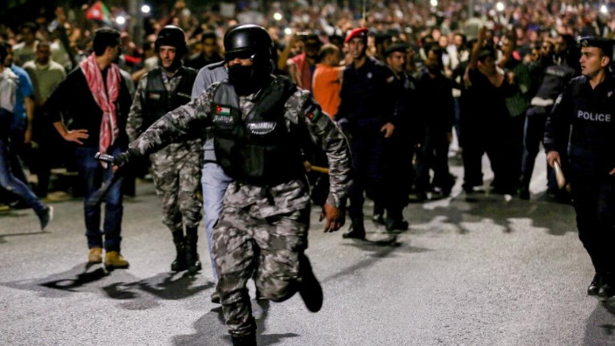 A member of the Jordanian gendarmerie runs as riot police stand on guard before protesters during a demonstration outside the Prime Minister's office in the capital Amman late on June 2, 2018. 
Khalil MAZRAAWI / AFP