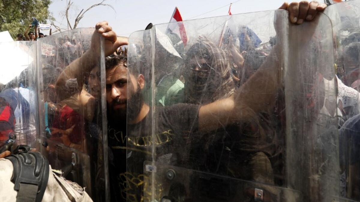 A protester grabs the shields of Iraqi security forces forming a human barrier, during a demonstration against unemployment and a lack of basic services, in the southern Iraqi city of Basra on July 15, 2018. (AFP/Haidar Mohammad Ali)