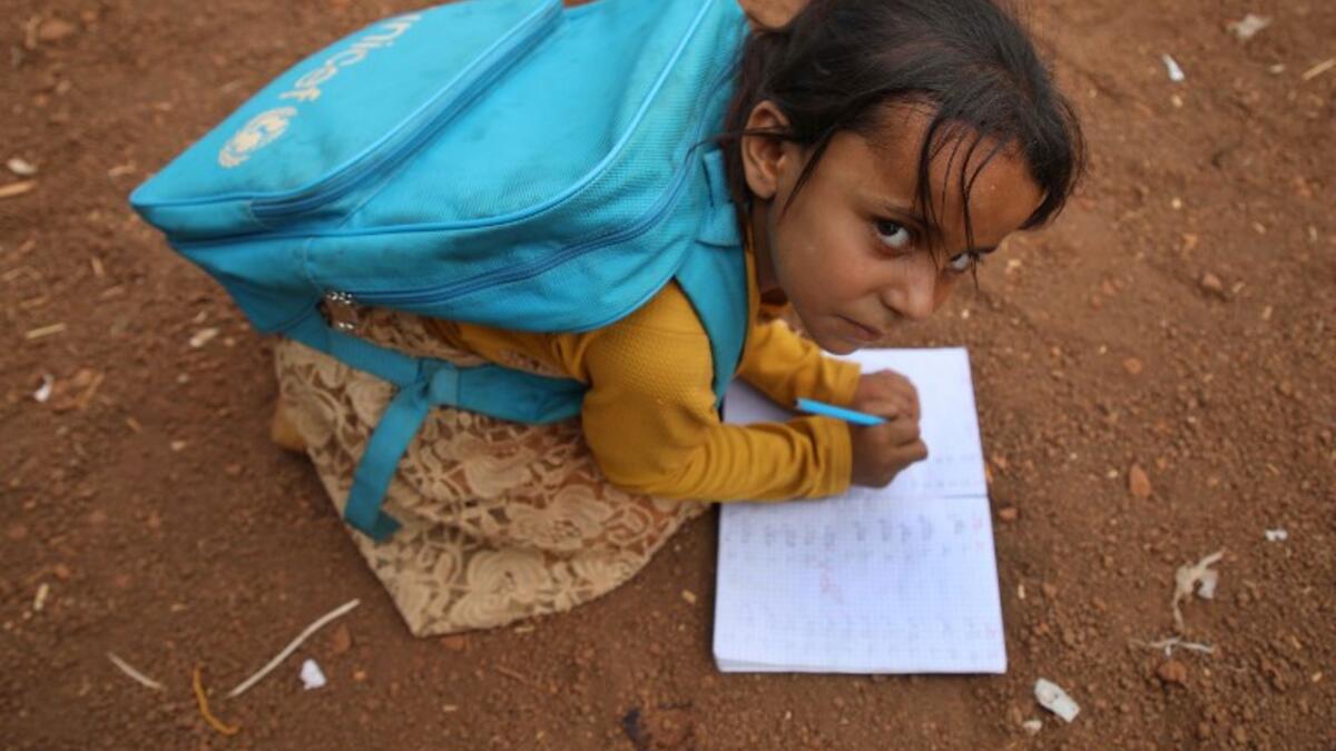 A Syrian child who fled with her family from the northern countryside of Hama, writes in a notebook in the yard of the makeshift school of "Zuhur al-Mustaqbal" (in Arabic "Flowers of the Future") in al-Jeneinah camp Aaref WATAD / AFP