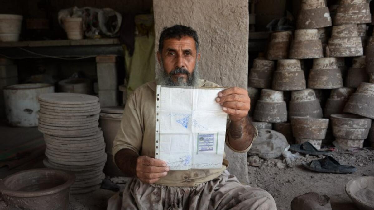 In this photo taken on October 10, 2018.Afghan potter Shirin Agha, 45, poses for a picture as he holds his id card or Tazkira registered to vote in the upcoming parliamentary election at his workshop, on the outskirts of Jalalabad. 
NOORULLAH SHIRZADA / AFP