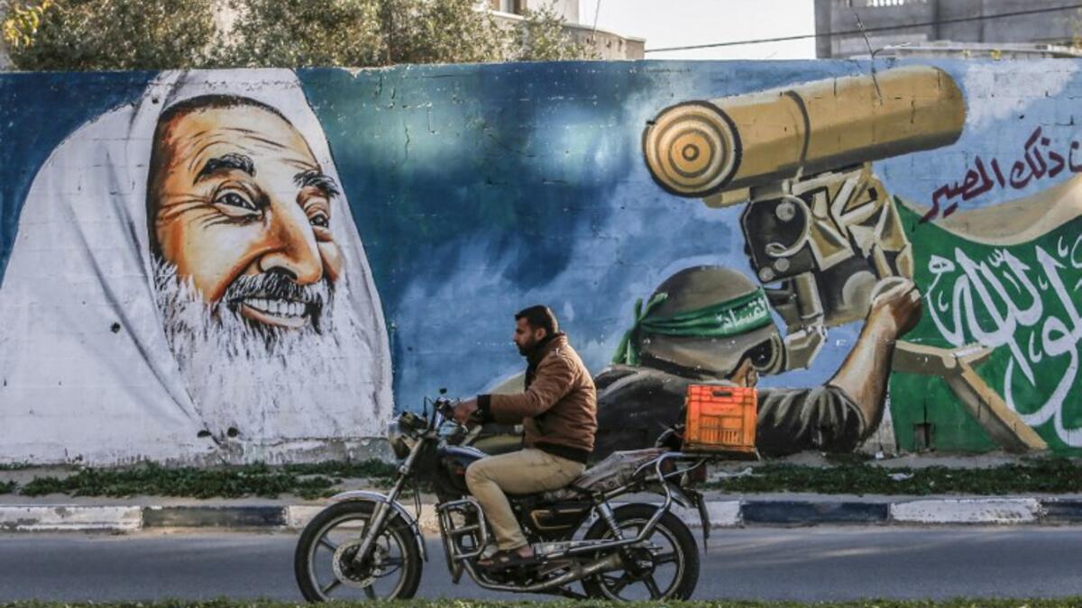 A Palestinian drives a motorcycle past a mural depicting late Hamas spiritual leader Sheikh Ahmed Yassin and a masked fighter of the Qassam Brigades, the armed wing of the Hamas movement, manning a turret alongside a street in Rafah in the southern Gaza Strip 
SAID KHATIB / AFP