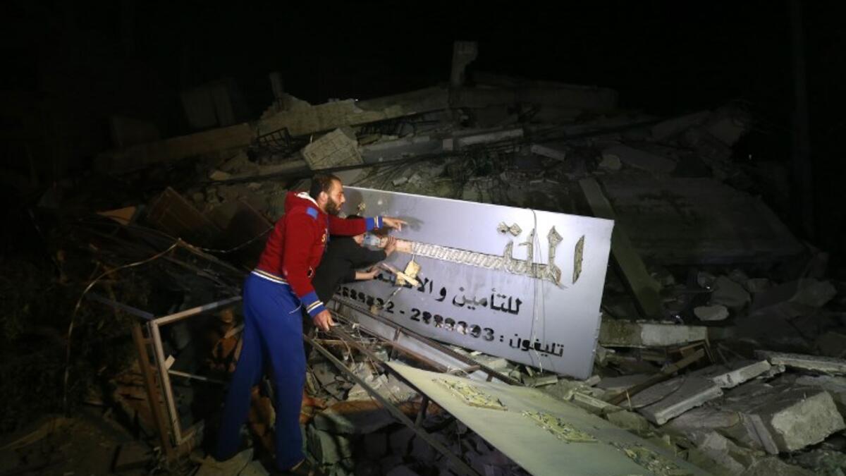 Palestinian men point at an insurance company sign amid the rubble of a building that collapsed from reported Israeli strikes in Gaza City on March 25, 2019. 
MOHAMMED ABED / AFP
