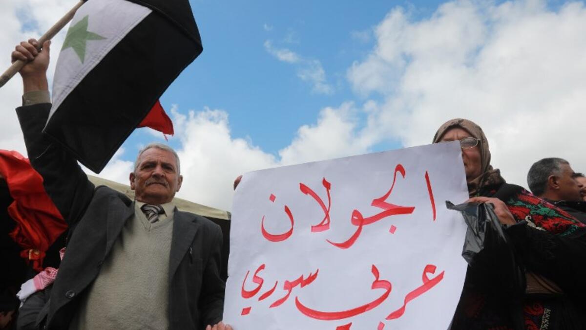 Protesters hold a national flag and a placard in the town of Quneitra in the Syrian occupied Golan Heights, during a demonstration against the US decision to recognise Israel's sovereignty over the Israeli-annexed Golan Heights, on March 26, 2019. The placard reads in Arabic: "The Golan is Arab and Syrian". 
Louai Beshara / AFP
