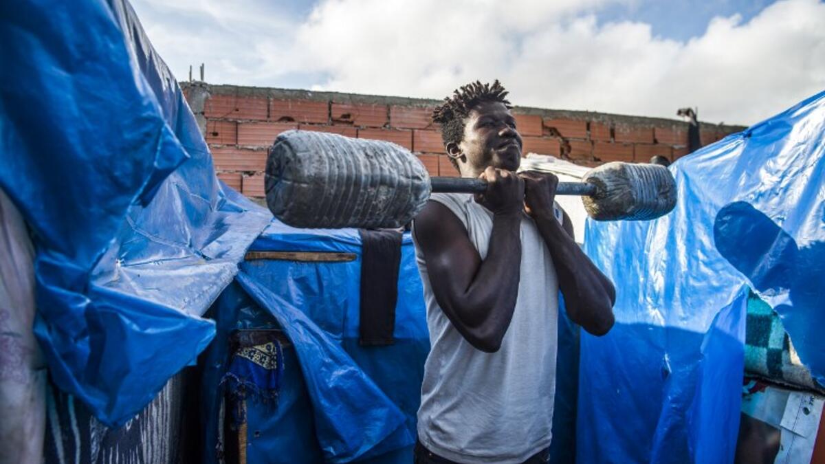 A sub-Saharan migrant lifts weights with a make-shift barbell between make-shift tents in the Oulad Ziane migrant camp in Casablanca on March 27, 2019. 
FADEL SENNA / AFP