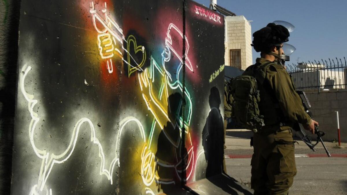 Israeli forces stand guard in front of a mural at the main entrance of Bethlehem, in the Israeli occupied West Bank as protests continue in the region.
(Musa AL SHAER / AFP)