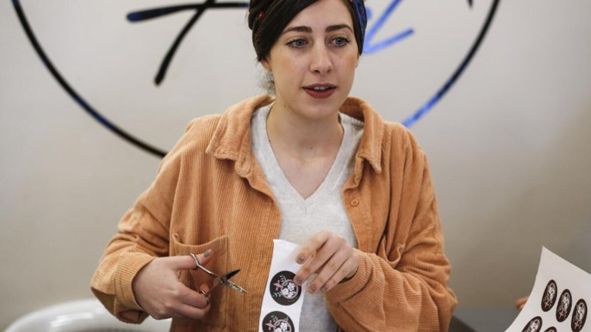 Amira Khader (L), Palestinian creative director of the feminist fashion label "BabyFist", cuts stickers while founder Yasmeen Mjalli stands next to her in their shop in Ramallah 
ABBAS MOMANI / AFP