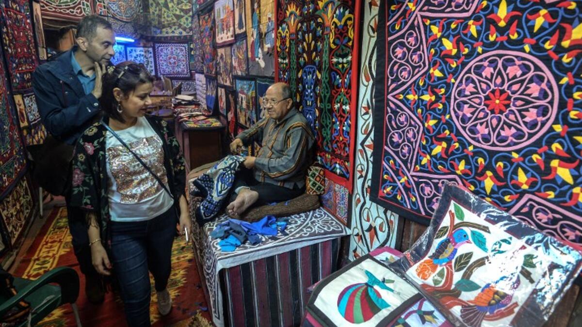 Customers walk in the shop of an Egyptian craftsman as he weaves a tapestry in his shop in Khayamiya Street, or the Street of Tent-makers, in the old city of the Egyptian capital Cairo on December 18, 2018. 
Mohamed el-Shahed / AFP