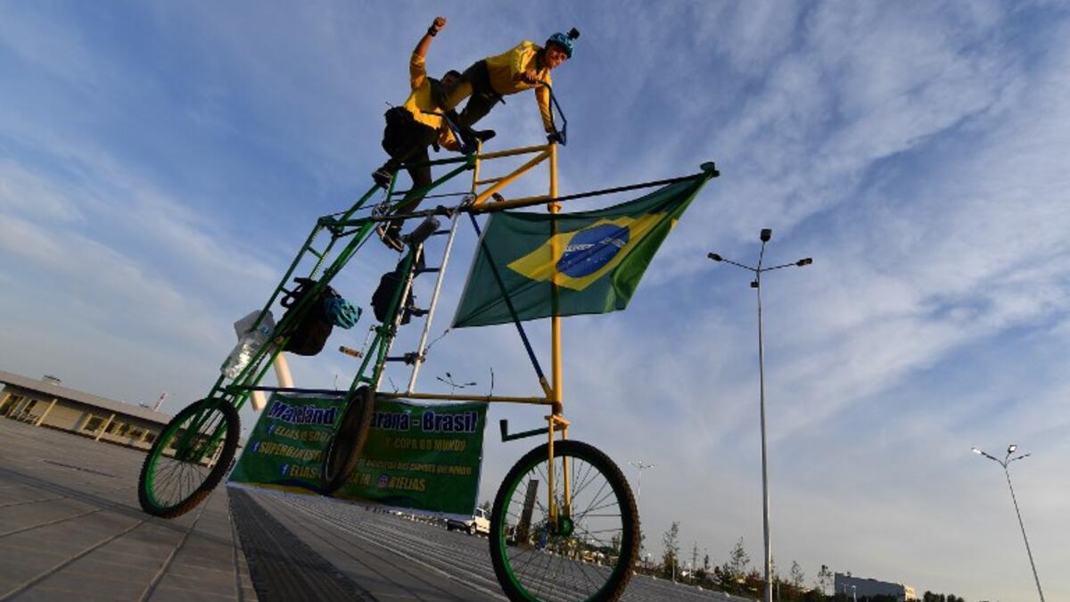 Brazilian football fans Elias de Souza and his son Elias de Souza junior perform acrobatics as they ride their homemade 3 metre-high tandem bicycle near Rostov Arena in Rostov-on-Don on June 16, 2018, on the eve of the match between Brazil and Switzerland during the Russia 2018 FIFA World Cup football tournament. 
JOE KLAMAR / AFP