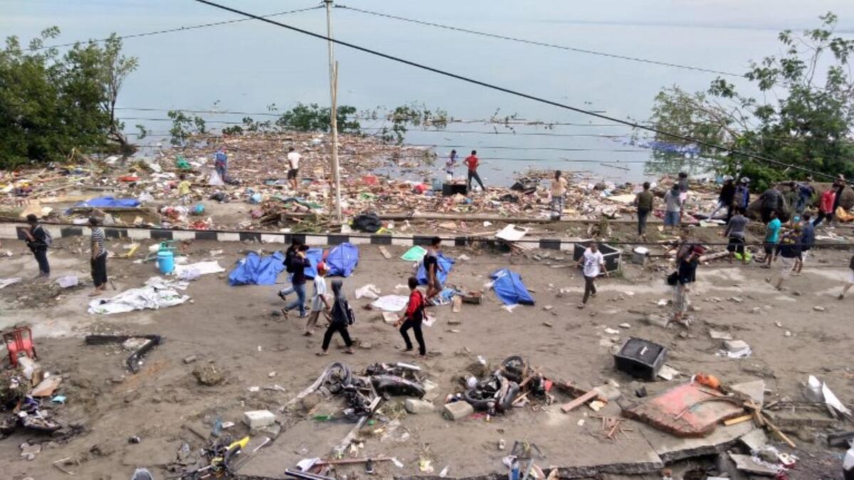 People walk past dead bodies (blue cover) a day after an earthquake and a tsunami hit Palu, on Sulawesi island on September 29, 2018. (OLA GONDRONK / AFP)