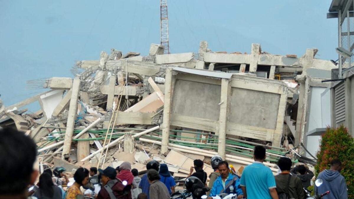 Residents gather to look at a collapsed building after an earthquake and tsunami hit Palu on Sulawesi island on September 29, 2018. (MUHAMMAD RIFKI / AFP)