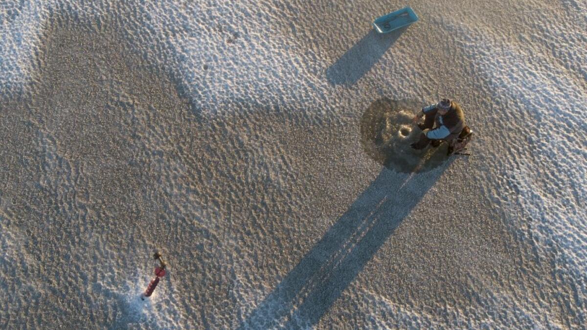 An aerial view shows a man sitting near a hole drilled into the frozen sea using an auger (L), as he ice fishes on the Gulf of Bothnia, near Vaasa, Western Finland on December 28, 2018, where winter daylight last for some four hours. 
Olivier MORIN / AFP