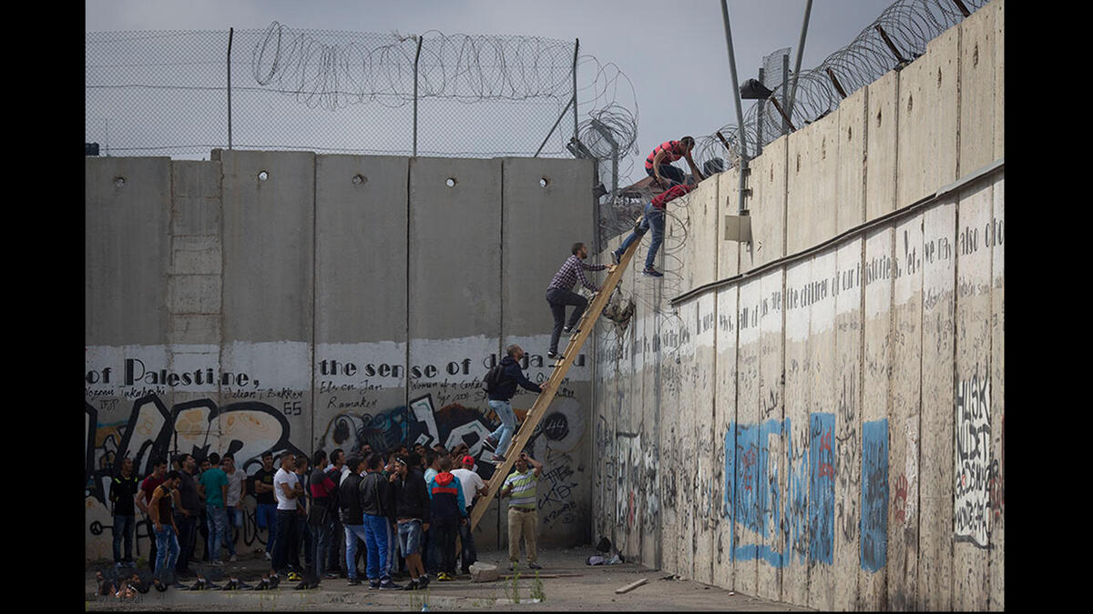 Palestinians climb over the barrier wall