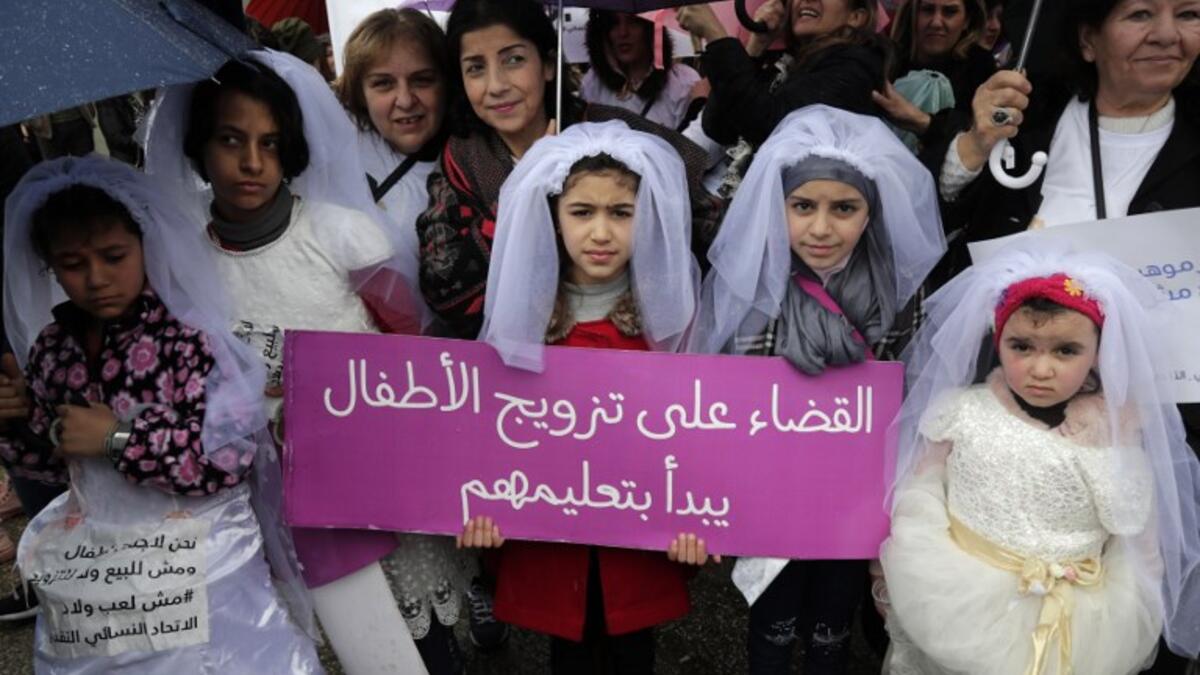 Young Lebanese girls disguised as brides hold a placard as they participate in a march against marriage before the age of 18, in the capital Beirut on March 2, 2019. The placard in Arabic reads "The end of child marriage begins by educating them". 
ANWAR AMRO / AFP