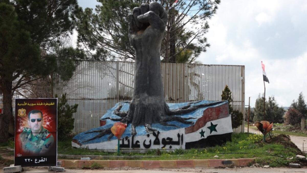 A portrait of the Syrian President Bashar al-Assad stands near a sculpture in the Syrian town of Quneitra, in the Golan Heights on March 26, 2019. The writing in Arabic reads: "The Golan is ours". 
Louai Beshara / AFP