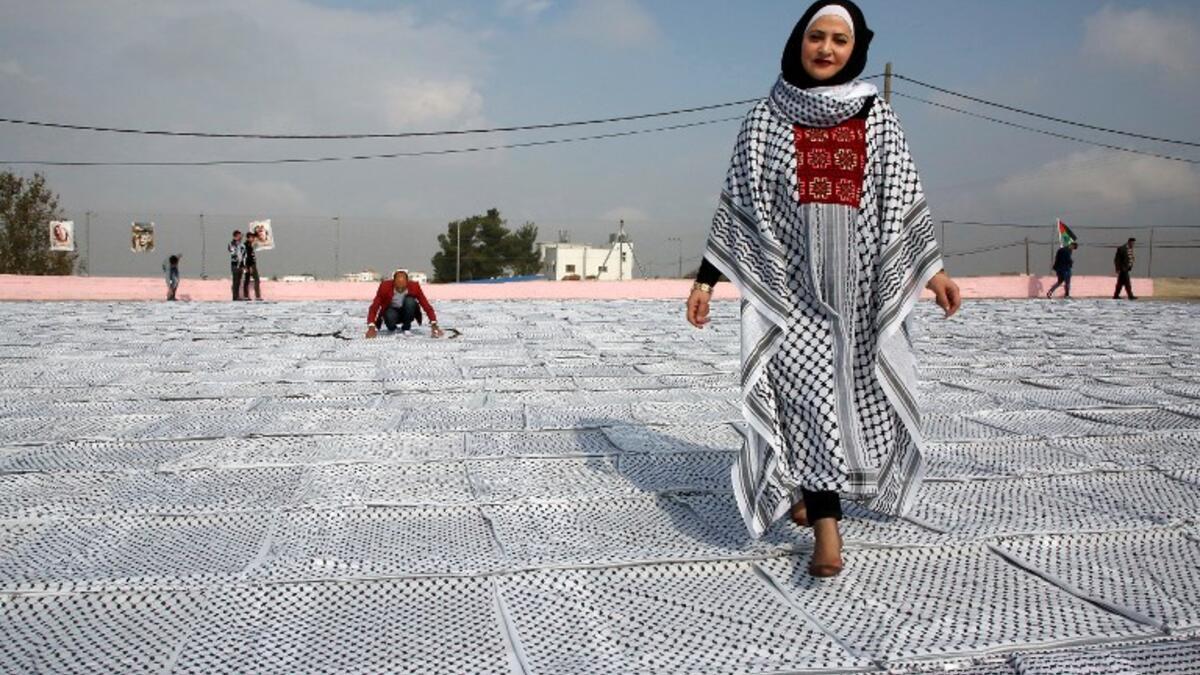 Palestinian Southern Education Direction's member Safa'a Amro (R) prepares a one thousand four hundred Meter square Keffiyeh. (HAZEM BADER / AFP)
