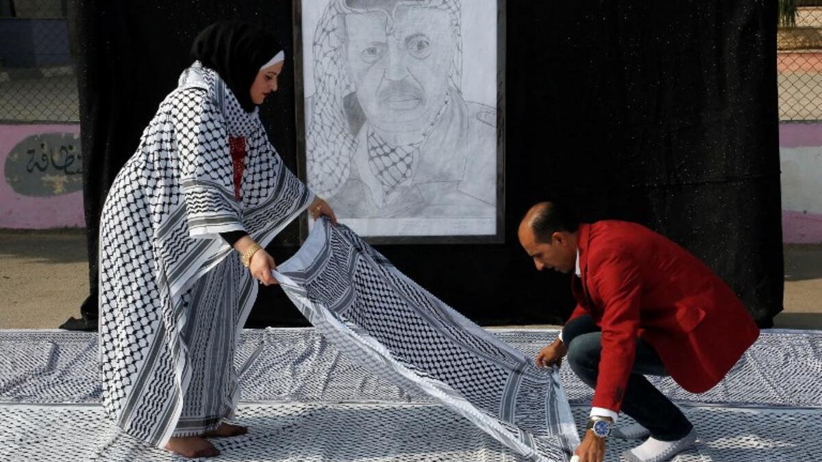 Palestinian Southern Education Direction's member Safa'a Amro (L) prepares a one thousand four hundred Meter square Keffiyeh (named "Arafatian" after the late Palestinian leader) to apply for the Guinness book of World Records' largest Keffiyeh in dura. (HAZEM BADER / AFP)