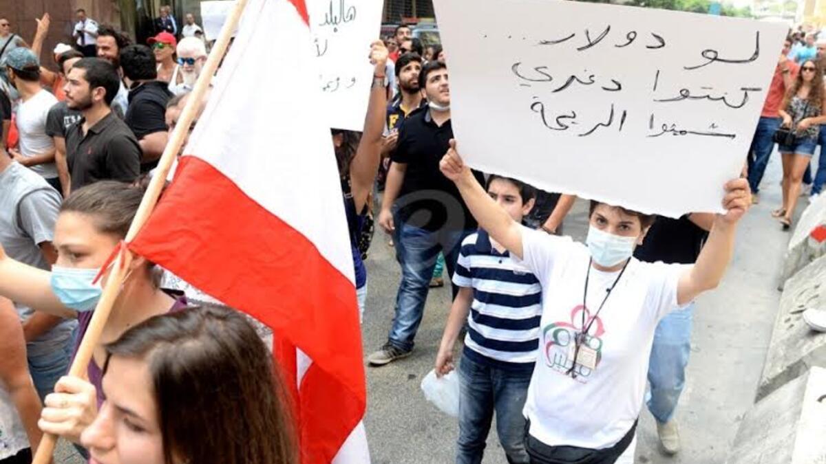 متظاهر يضع كمامة بسبب ريحة القمامة ويحمل شعار "لو دولار كنتوا دغري شميتوا الريحة" واصفاً أن المسؤوليين لم يهتموا برائحة القمامة ولو هناك فائدة مادية لكانوا تحركوا.