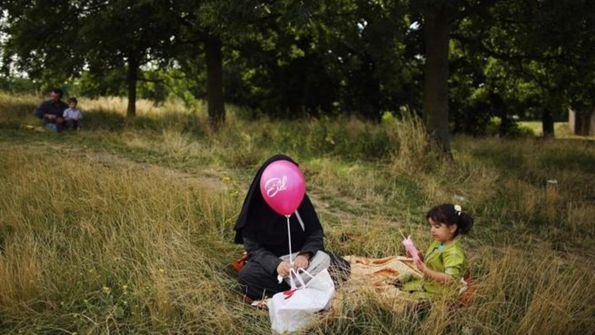 A woman and girl sit in the shade in Burgess Park during an Eid celebration fun fair in London, England. (GETTY)