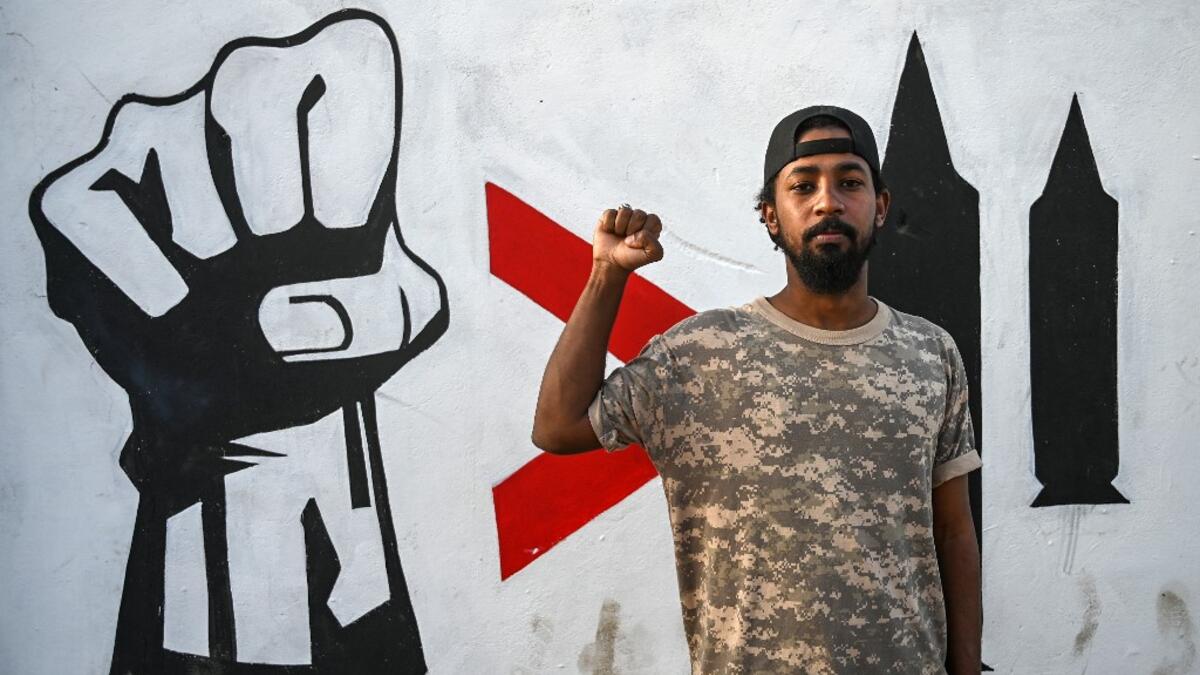 Sudanese graffiti artist Amir Saleh poses in front of a recently painted mural made by his team during a protest near the army headquarters in the capital Khartoum (AFP)