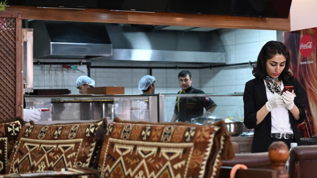 An Afghan waitress checks her smartphone at an Afghan Kebab restaurant at Esenyurt district in Istanbul.  OZAN KOSE / AFP