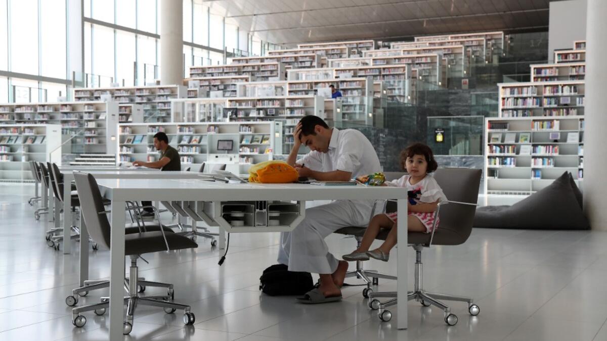 A youth works while seated at a table with a toddler inside the Qatar National Library in the capital Doha.  KARIM JAAFAR / AFP