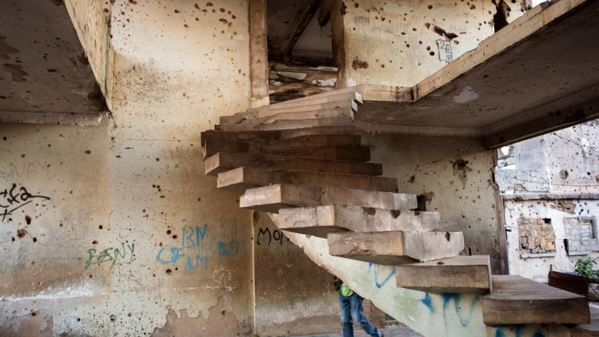 A person walks past a staircase in the bullet-riddled and graffiti-covered shell of a building that used to house Jonas Savimbi, leader of the rebel UNITA movement  RODGER BOSCH / AFP