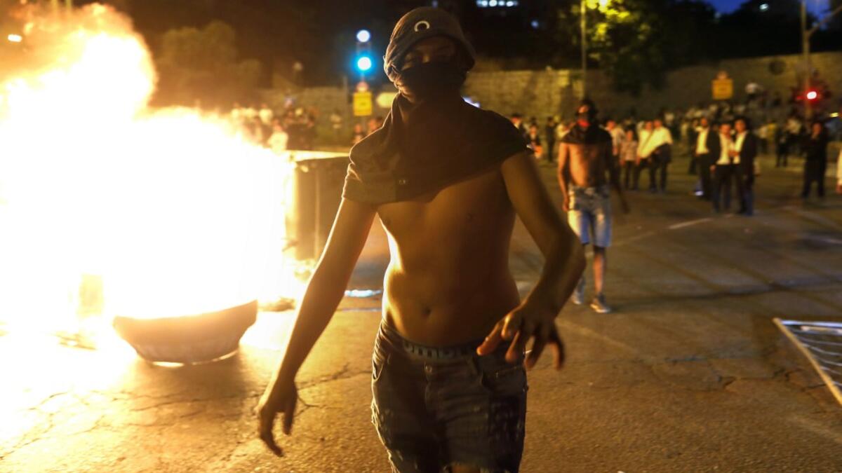 A masked Israeli member of the Ethiopian community walks past a burning barrier blocking the main entrance to Jerusalem, to protest the killing of Solomon Tekah, a young man of Ethiopian origin who was killed by an off-duty police officer.  MENAHEM KAHANA / AFP