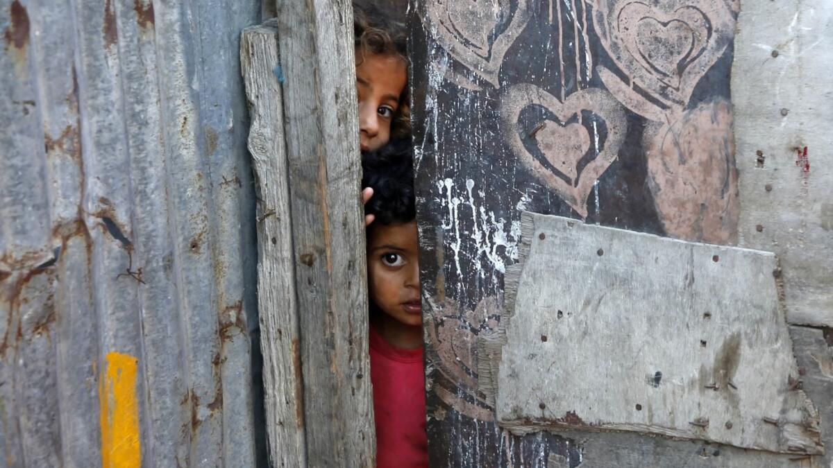 Palestinian children peep from behind a makeshift door at an empoverished neighbourhood in Gaza City on July 4, 2019.  MOHAMMED ABED / AFP