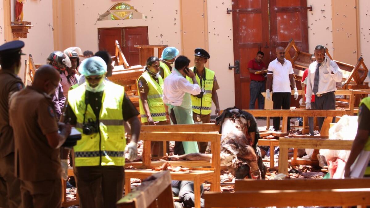 Sri Lankan security personnel walk past debris next to a dead body slumped over a bench following an explosion in St Sebastian's Church in Negombo, north of the capital Colombo, on April 21, 2019. STR / AFP