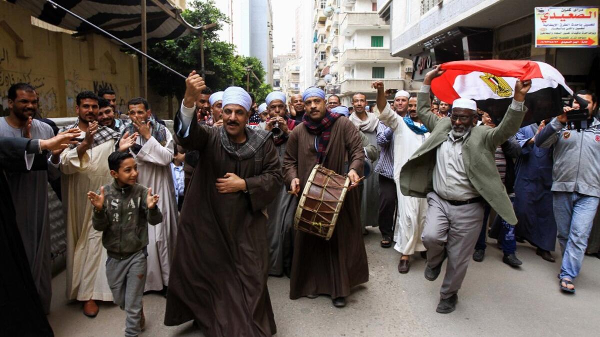 An Egyptian man dances with a national flag as others play musical instruments while walking in a procession outside a school in the second city of Alexandria, during voting in a referendum on constitutional amendments. Tarek ABDEL HAMID / AFP